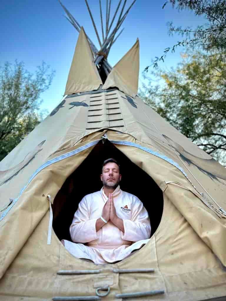 Jonathan Thompson sitting with hands in prayer in a teepee wearing a bathrobe, Scottsdale, Arizona
