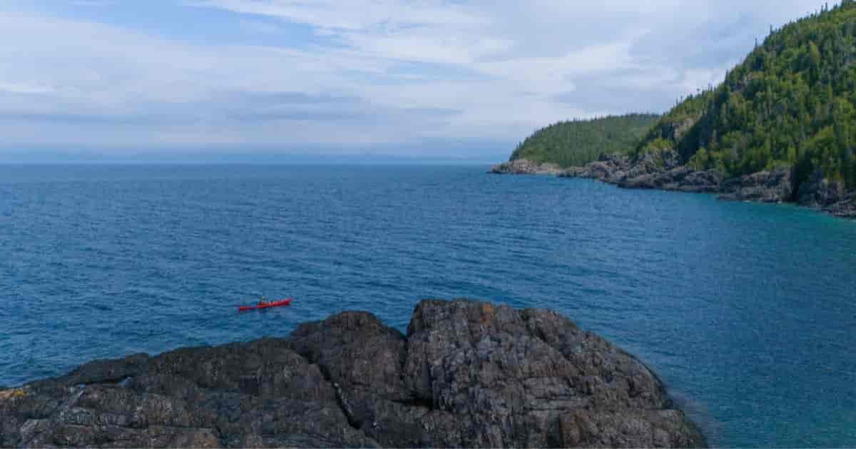 Ken Whiting paddling a kayak across the calm, clear waters of Lake Superior, surrounded by water and forests.